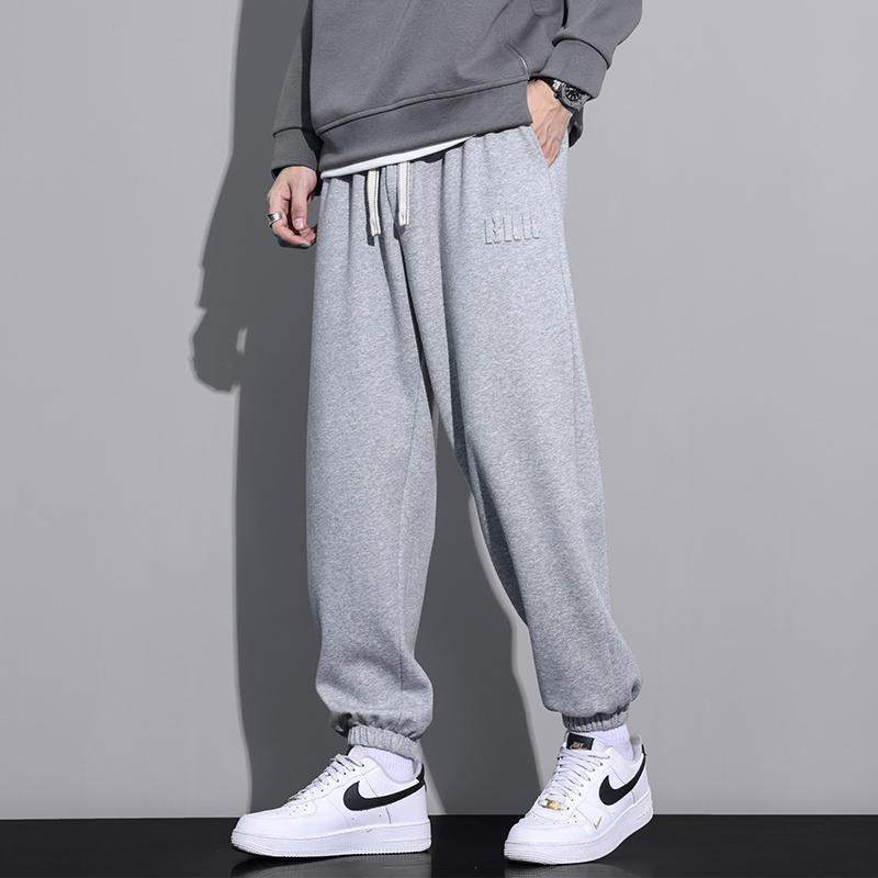 Pantaloni tuta grigi uomo, stile casual, abbinati a felpa grigia e scarpe sportive bianche Nike. Look moderno e confortevole.