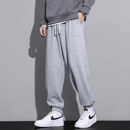 Pantaloni tuta grigi uomo, stile casual, abbinati a felpa grigia e scarpe sportive bianche Nike. Look moderno e confortevole.