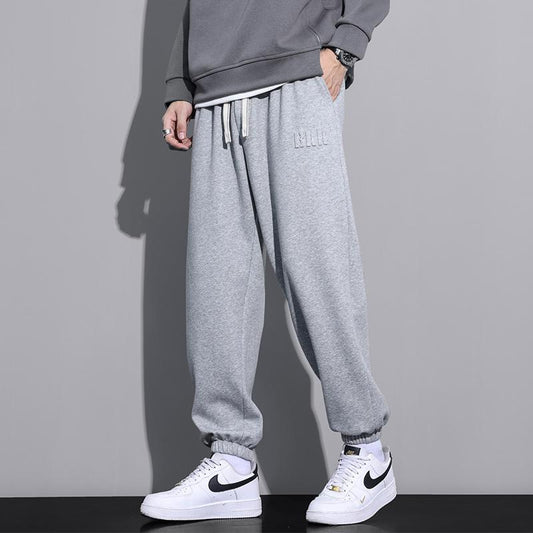Pantaloni tuta grigi uomo, stile casual, abbinati a felpa grigia e scarpe sportive bianche Nike. Look moderno e confortevole.