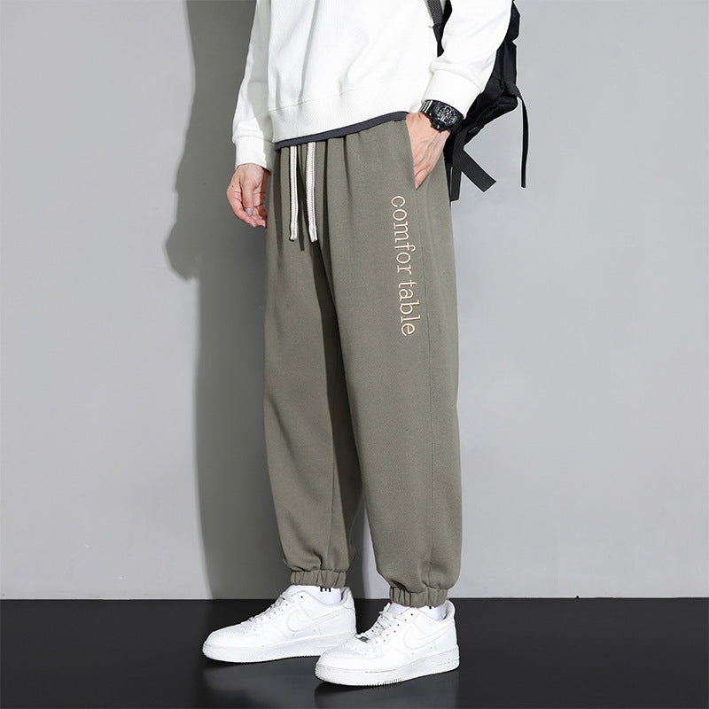 Pantaloni jogger grigi da uomo con scritta "comfortable", abbinati a felpa bianca e scarpe da ginnastica bianche, moda casual e sportiva.