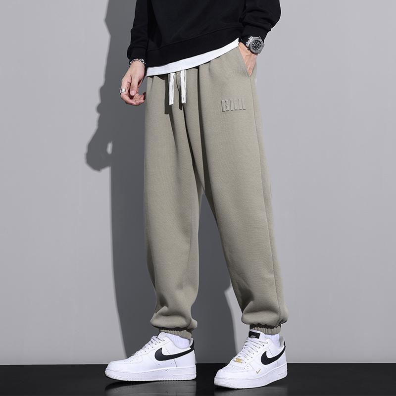 Pantaloni jogger grigi da uomo, abbinati a sneakers bianche Nike, su sfondo grigio. Moda casual, abbigliamento sportivo, stile urbano.