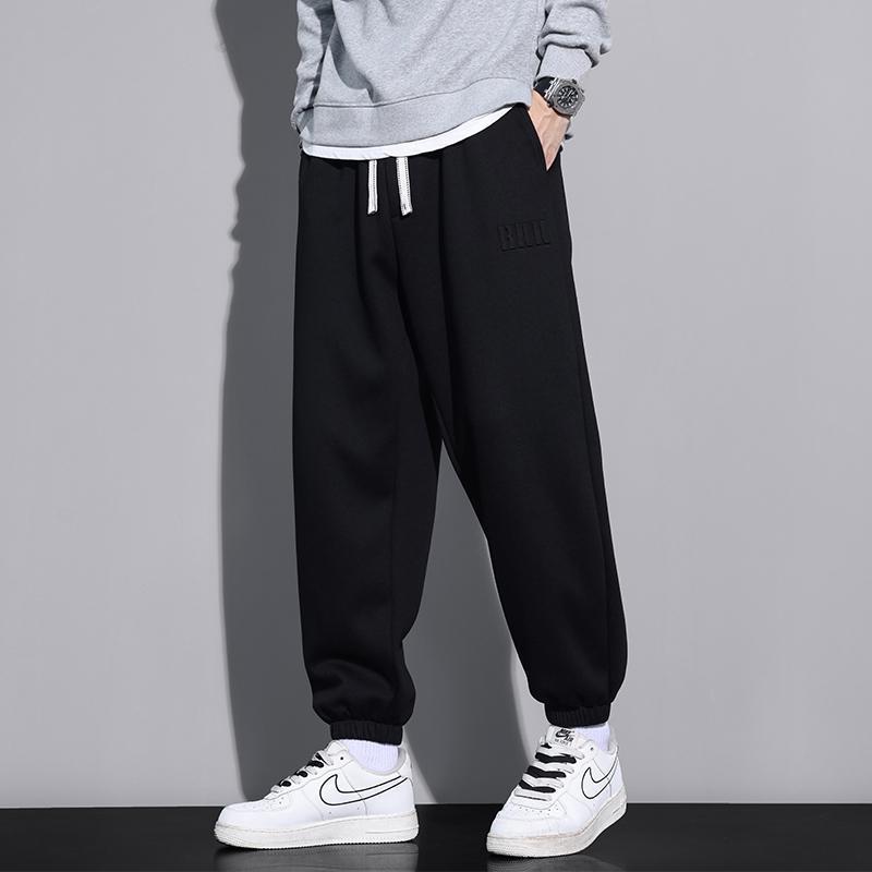 Pantaloni jogger neri da uomo, stile casual, abbinati a scarpe sportive bianche Nike e felpa grigia. Moda streetwear, comfort quotidiano.