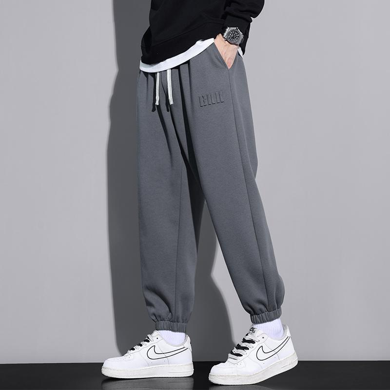 Pantaloni jogger grigi da uomo, abbinati a scarpe da ginnastica bianche Nike, su sfondo grigio. Stile casual, moda streetwear.
