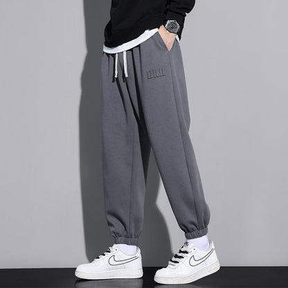 Pantaloni jogger grigi da uomo, abbinati a scarpe da ginnastica bianche Nike, su sfondo grigio. Stile casual, moda streetwear.