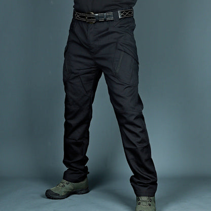Pantaloni tattici neri con tasche multiple, indossati con cintura robusta e scarpe militari verdi. Abbigliamento outdoor resistente e funzionale.