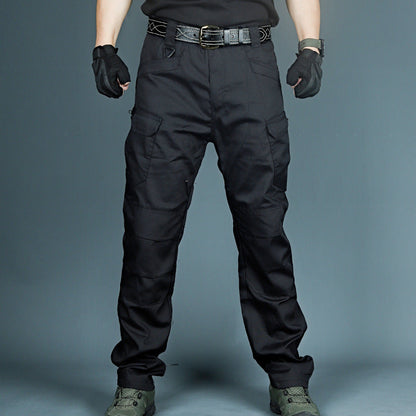 Pantaloni tattici neri con tasche cargo, guanti e scarpe militari. Abbigliamento outdoor resistente, ideale per escursionismo e attività all'aperto.