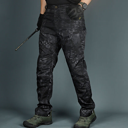 Pantaloni tattici neri con motivo mimetico, indossati con guanti e scarpe da trekking verdi. Ideali per attività outdoor e avventure militari.