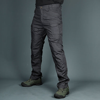 Pantaloni tattici grigi con tasche multiple, indossati con scarpe da trekking verdi. Abbigliamento outdoor resistente e funzionale per escursioni.
