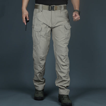 Pantaloni tattici beige con tasche multiple, indossati da una persona in piedi su sfondo grigio. Ideali per attività outdoor e avventure.