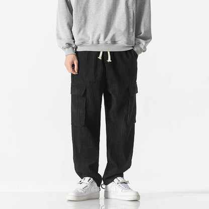 Pantaloni cargo neri in velluto a coste, indossati con felpa grigia e sneakers bianche. Stile casual maschile, moda urbana autunnale.