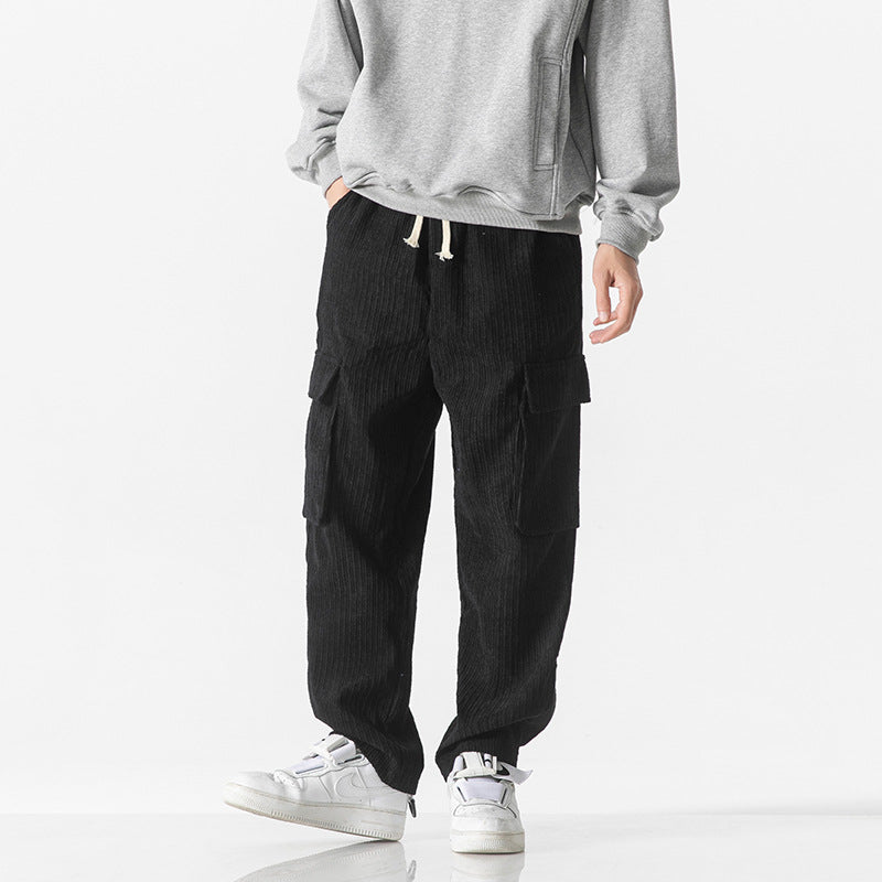 Pantaloni cargo neri in velluto a coste, indossati con felpa grigia e sneakers bianche. Stile casual, moda uomo, abbigliamento autunnale.