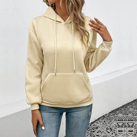 Donna con felpa beige con cappuccio e jeans, posa casual. Moda autunnale, abbigliamento comodo, stile urbano. Sfondo bianco minimalista.