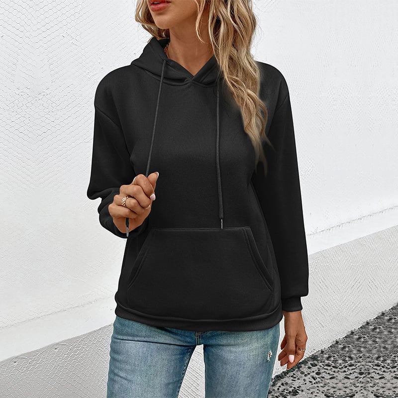 Donna con felpa nera con cappuccio e jeans, posa casual su sfondo bianco. Moda streetwear, abbigliamento casual femminile, stile urbano.