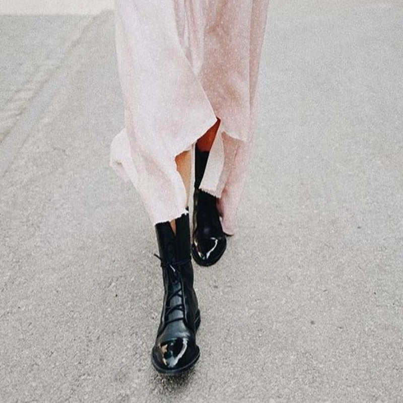 Stivali neri lucidi con abito rosa lungo su strada grigia. Moda autunnale, stile urbano, tendenze calzature donna.