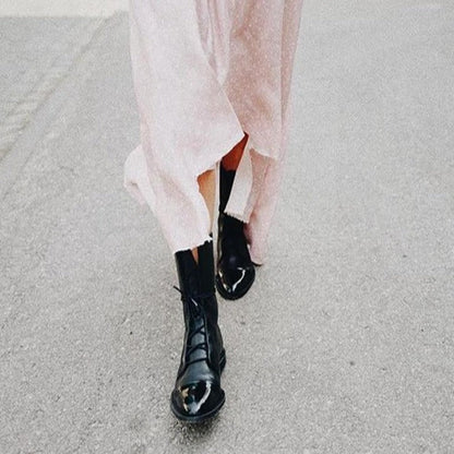 Stivali neri lucidi con abito rosa lungo su strada grigia. Moda autunnale, stile urbano, tendenze calzature donna.