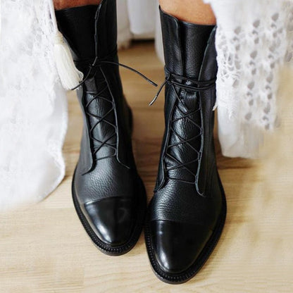 Stivali neri in pelle con lacci su pavimento in legno, indossati con abito bianco in pizzo. Scarpe eleganti e moderne per look autunnale.