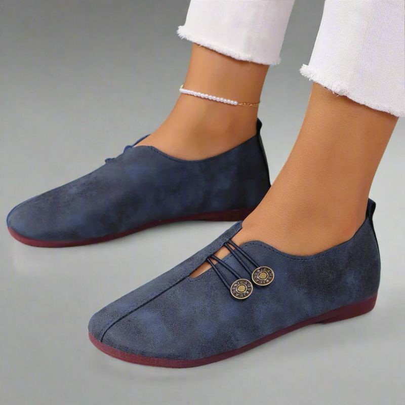 Scarpe donna blu scamosciate, design casual con bottoni decorativi, indossate con pantaloni bianchi. Calzature moda comode ed eleganti.
