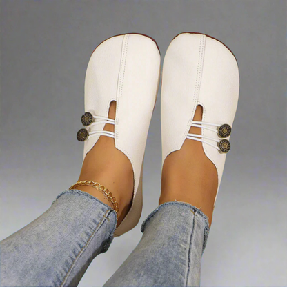 Scarpe bianche in pelle con bottoni decorativi, indossate con jeans chiari. Calzature eleganti e comode per donna, moda casual chic.