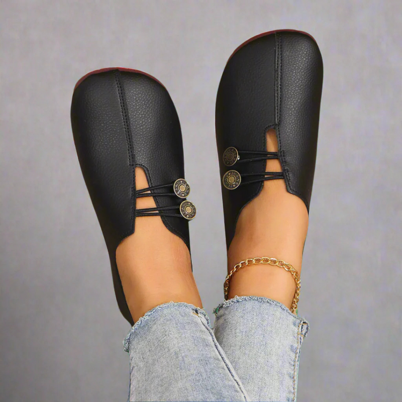 Scarpe mocassini neri in pelle con bottoni decorativi, indossate con jeans chiari. Design elegante e moderno, perfetto per moda casual.