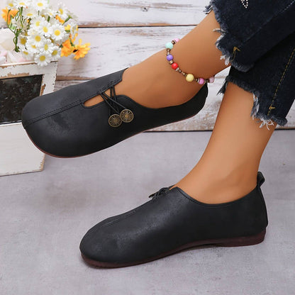 Scarpe nere in pelle con lacci, indossate da una persona con jeans strappati e cavigliera colorata. Sfondo con fiori bianchi.