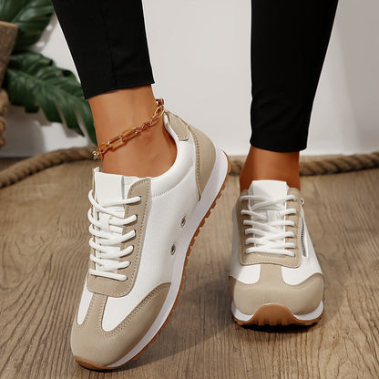 Scarpe da ginnastica bianche e beige su pavimento in legno, indossate con pantaloni neri. Design moderno, suola in gomma, perfette per look casual.