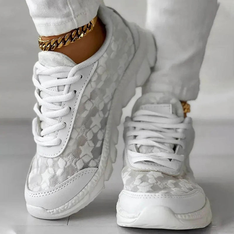 Scarpe da ginnastica bianche eleganti con dettagli in pizzo floreale, indossate con pantaloni bianchi. Stile moderno, moda casual, accessori dorati.