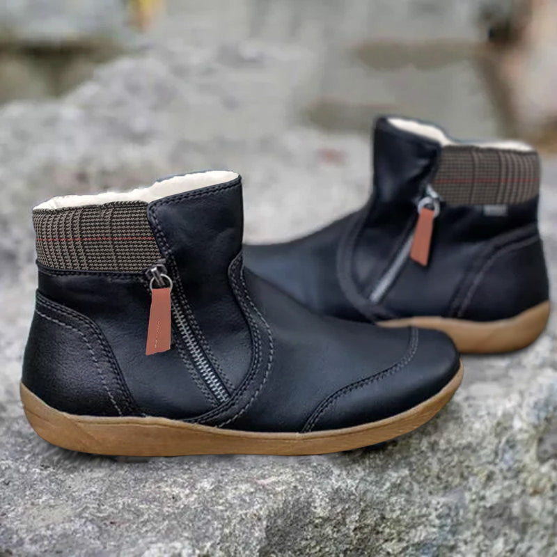 Stivaletti neri in pelle con cerniera laterale, suola marrone e fodera interna calda, posizionati su sfondo roccioso. Scarpe invernali eleganti e comode.