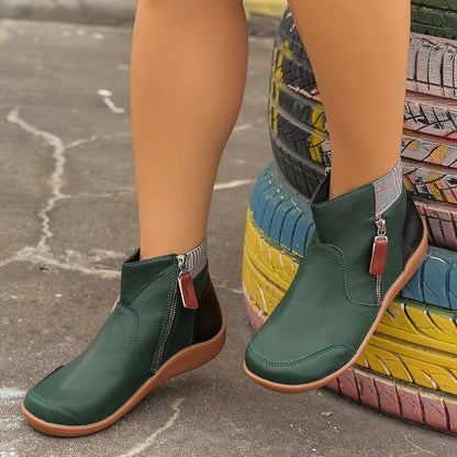 Stivaletti verdi in pelle con cerniera laterale, suola marrone chiaro, indossati su strada asfaltata. Scarpe moda autunno, stile casual elegante.