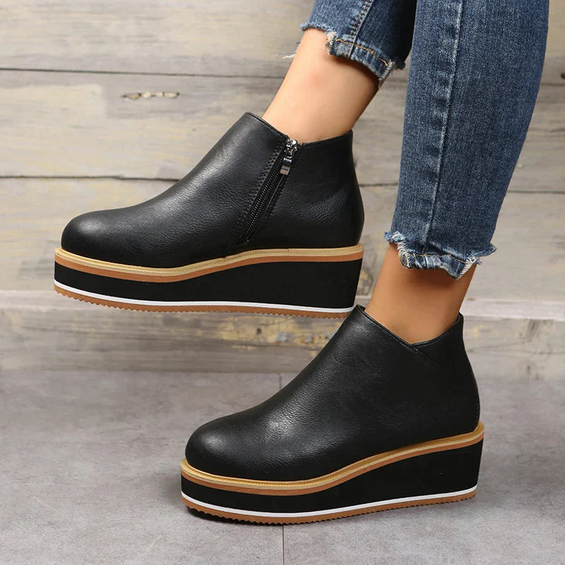 Scarpe platform nere in pelle con cerniera laterale, indossate con jeans strappati. Calzature moda donna, tendenza autunno, suola alta.
