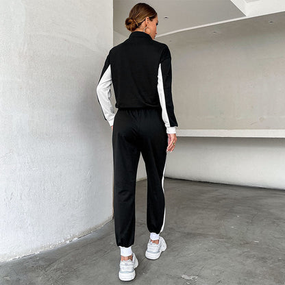 Donna in tuta sportiva nera e bianca, vista di spalle, in un ambiente minimalista. Indossa scarpe da ginnastica bianche.
