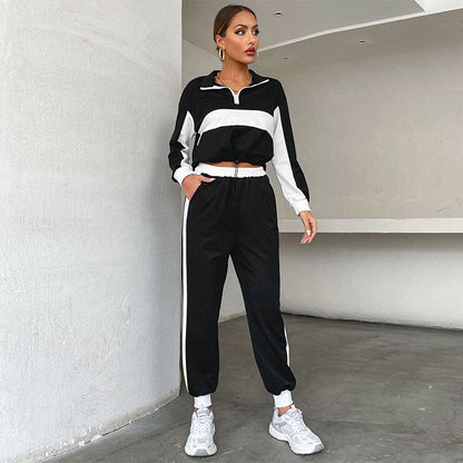 Donna in tuta sportiva nera e bianca, scarpe da ginnastica bianche, posa in un ambiente moderno. Abbigliamento casual, moda donna, stile athleisure.
