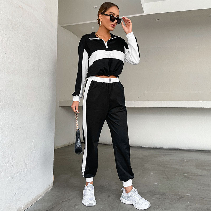 Donna con tuta sportiva bianca e nera, occhiali da sole e borsa nera, posa in un ambiente minimalista. Moda casual, abbigliamento sportivo trendy.