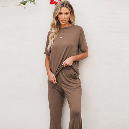 Donna con abbigliamento casual marrone, maglietta e pantaloni coordinati, posa davanti a sfondo chiaro. Moda donna, stile rilassato, tendenza 2023.