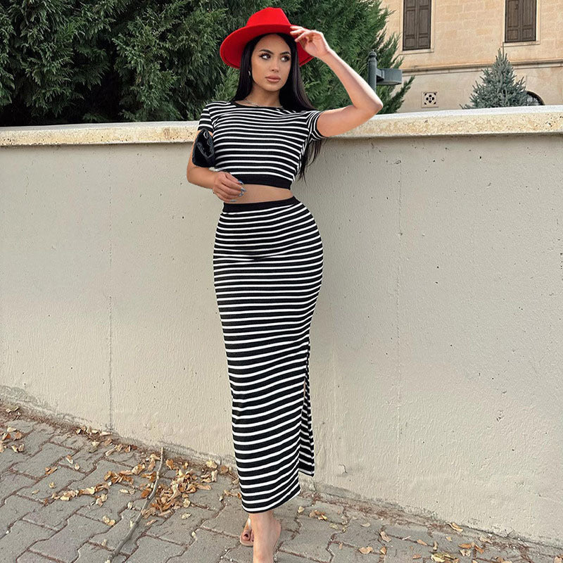 Donna con abito a righe bianche e nere, cappello rosso, appoggiata a un muro. Moda elegante, look estivo, stile urbano.