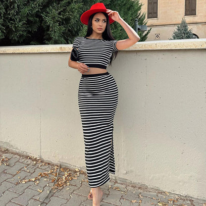 Donna con abito a righe bianche e nere, cappello rosso, appoggiata a un muro. Moda elegante, look estivo, stile urbano.