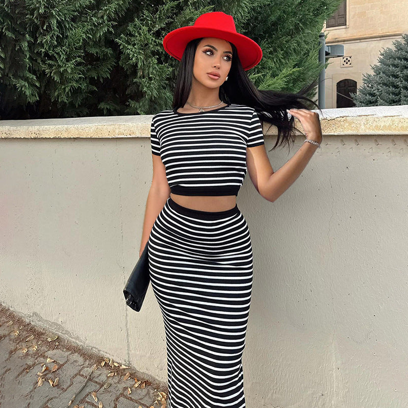 Donna con abito a righe bianche e nere e cappello rosso, appoggiata a un muro. Moda elegante, look estivo, accessori chic.
