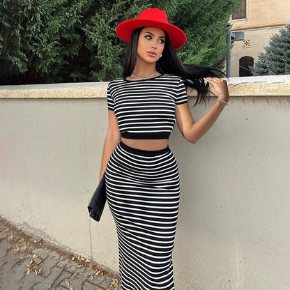 Donna con abito a righe bianche e nere e cappello rosso, appoggiata a un muro. Moda elegante, look estivo, accessori chic.