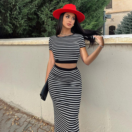 Donna con abito a righe bianche e nere e cappello rosso, appoggiata a un muro. Moda elegante, look estivo, accessori chic.