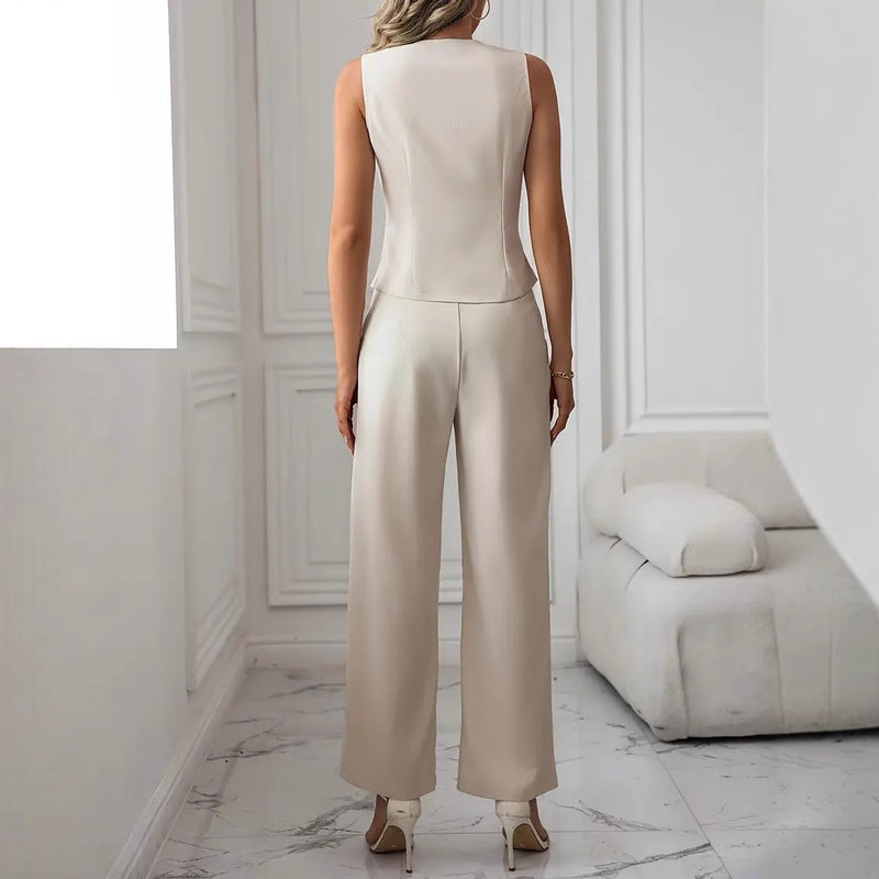Donna in elegante completo bianco, pantaloni larghi e top senza maniche, in un salotto moderno con divano bianco e pavimento in marmo.