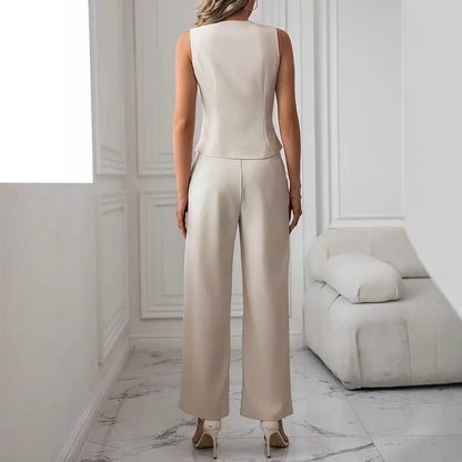 Donna in elegante completo bianco, pantaloni larghi e top senza maniche, in un salotto moderno con divano bianco e pavimento in marmo.