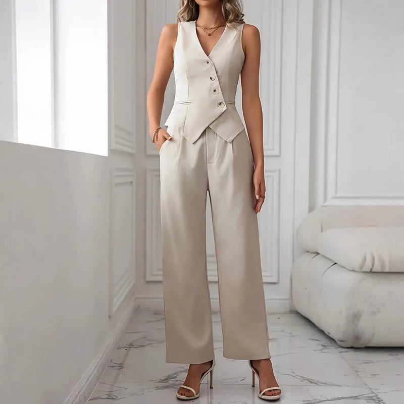 Donna in elegante completo beige con gilet e pantaloni, in piedi su pavimento in marmo bianco, interni moderni. Moda femminile, abbigliamento chic.