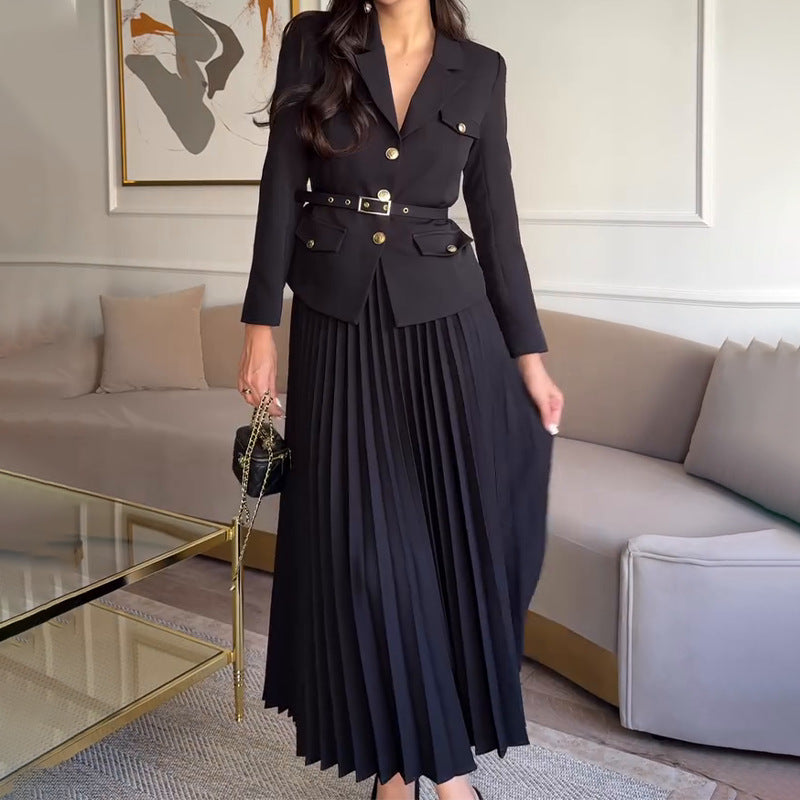 Donna in elegante abito nero con giacca a bottoni e gonna plissettata, in un salotto moderno. Moda femminile, abbigliamento chic, stile sofisticato.