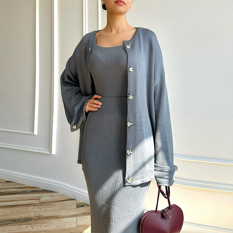 Donna in abito grigio elegante con cardigan abbinato, tiene una borsa a forma di cuore. Moda autunnale, stile sofisticato, abbigliamento femminile.