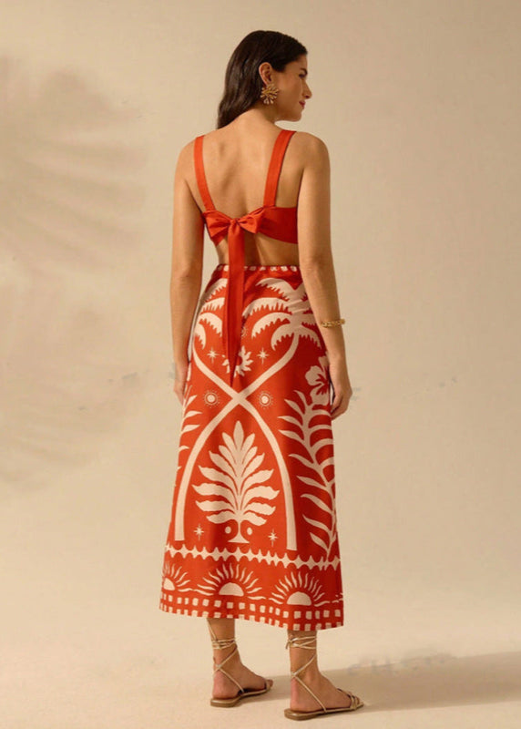 Donna di spalle con abito lungo rosso a motivi bianchi, sandali beige, sfondo neutro. Moda estiva, abbigliamento elegante, tendenze 2023.