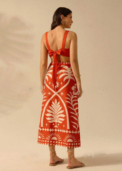Donna di spalle con abito lungo rosso a motivi bianchi, sandali beige, sfondo neutro. Moda estiva, abbigliamento elegante, tendenze 2023.