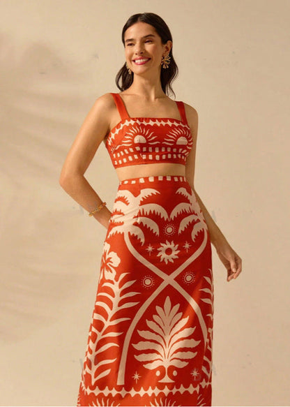 Donna sorridente in abito lungo rosso con motivi bianchi floreali e geometrici, sfondo neutro. Moda elegante, abbigliamento estivo, stile boho-chic.
