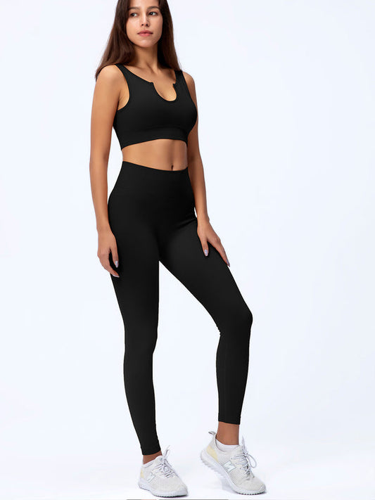 Donna in abbigliamento sportivo nero, top e leggings, posa su sfondo bianco. Indossa scarpe da ginnastica grigie. Fitness, moda, abbigliamento sportivo.