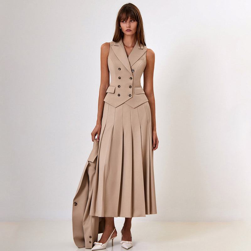 Donna in abito beige elegante senza maniche, con bottoni e gonna a pieghe, tiene una giacca abbinata. Scarpe bianche con tacco. Moda femminile chic.
