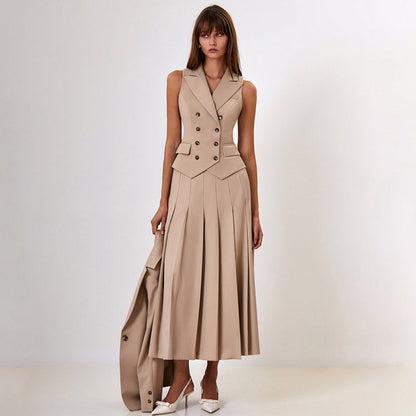 Donna in abito beige elegante senza maniche, con bottoni e gonna a pieghe, tiene una giacca abbinata. Scarpe bianche con tacco. Moda femminile chic.