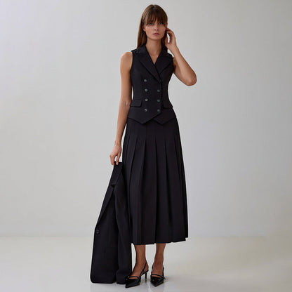 Donna in abito nero elegante con gilet e gonna lunga a pieghe, tacchi alti, su sfondo neutro. Moda femminile, abbigliamento formale, stile sofisticato.